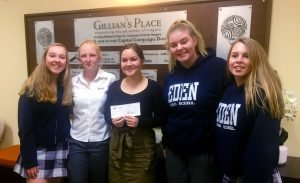 Four female students deliver a donation cheque to a charity representative.