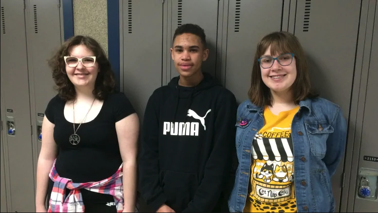 Three secondary school students from the YPI program stand in front of a row of lockers.