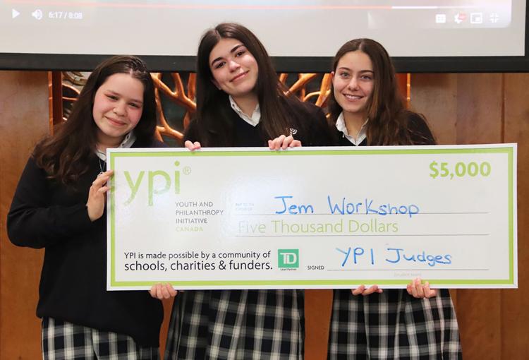 Trois étudiants détiennent un chèque surdimensionné de 5000 $ remis à Jem Workshop