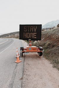 LED road sign on a highway curve that reads "Stay Home"